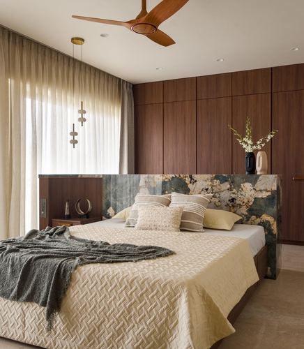 Bedroom with wood-panelled wall, patterned stone headboard, wooden ceiling fan and layered cream bedding