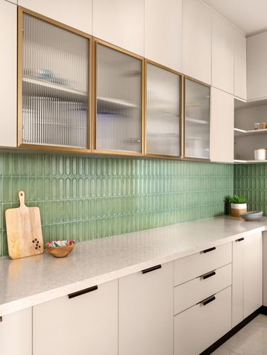 Kitchen counter with green scalloped tile backsplash and fluted glass, brass-framed upper cabinets