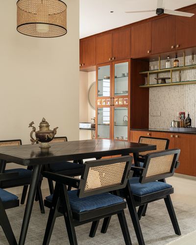 Dining room with cane-back chairs, black table, cane pendant light, and wooden cabinetry beyond