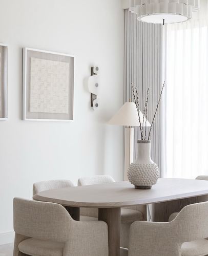 Neutral dining room with oval wood table, linen chairs, textured vase and framed art on wall