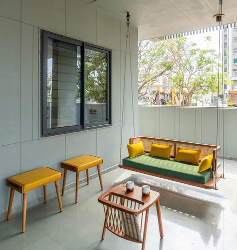 Balcony with cane swing, mustard stools, and city trees seen through sliding window