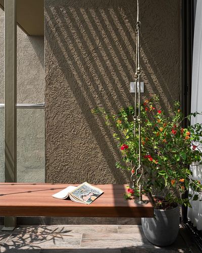 Wooden bench with open book beside potted flowering plant under striped sunlight on textured wall