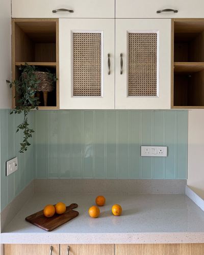 Kitchen corner with cane-front cabinets, green fluted backsplash, terrazzo counter and oranges on a wooden board