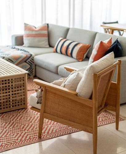 Cane-backed wooden armchair beside a grey sectional sofa with striped cushions on a terracotta patterned rug