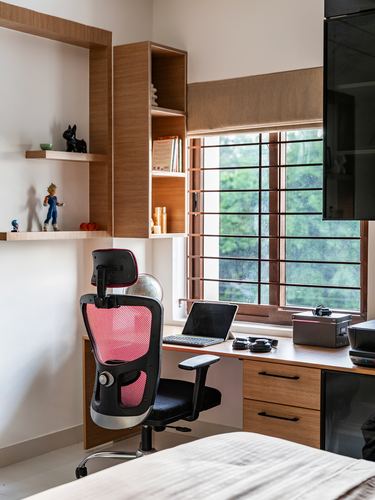 Study corner with wooden shelving, red mesh chair, desk facing window, in Hyderabad home
