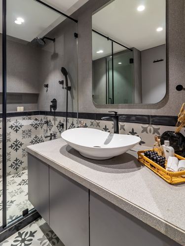 Grey bathroom with oval white vessel sink, black fixtures, and patterned cement tile shower wall