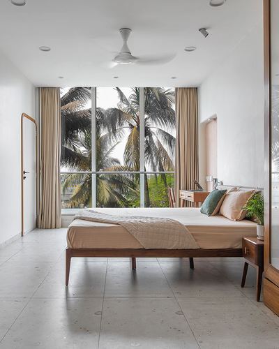 Minimalist bedroom with wood bed facing floor-to-ceiling window overlooking palm trees