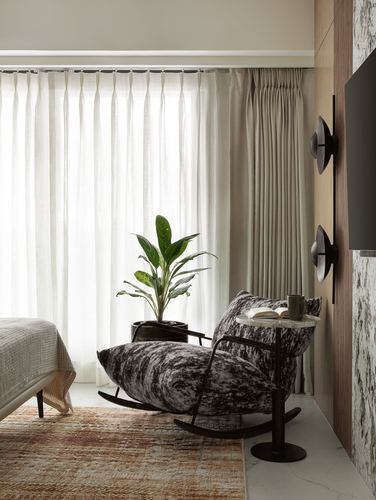 Bedroom corner with black rocking chair, marble side table, and sheer curtains beside a plant.