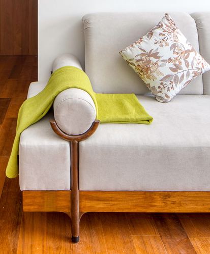 Close-up of a beige sofa with wooden armrest, green throw, and floral cushion on wood floor