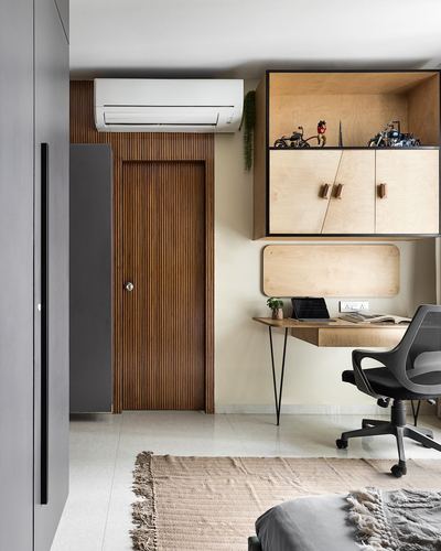 Bedroom corner with fluted wood door, wall-mounted plywood desk, open shelving, and grey wardrobe