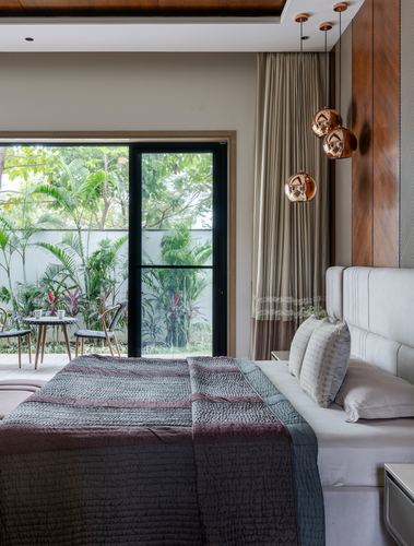 Bedroom with upholstered headboard, copper pendant cluster, and glass door opening to a green courtyard