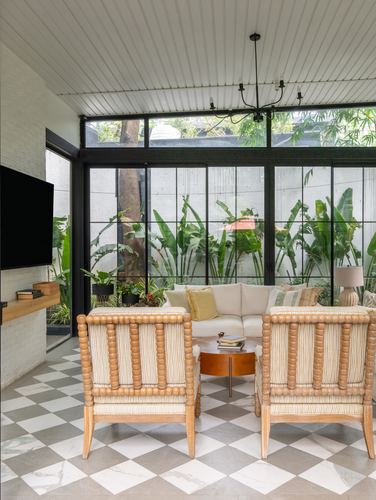 Living room with spool chairs, diamond marble floor, and floor-to-ceiling black windows facing garden