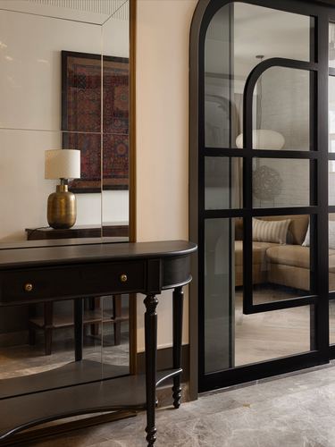 Black console table and mirror in foyer beside arched black-framed glass door opening to a living room.