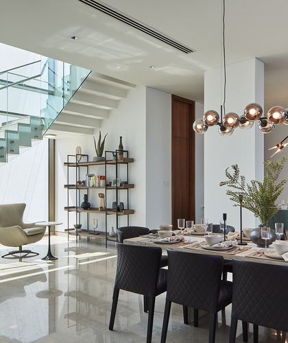 Open-plan dining area with quilted black chairs, globe pendant lights, and glass staircase beyond