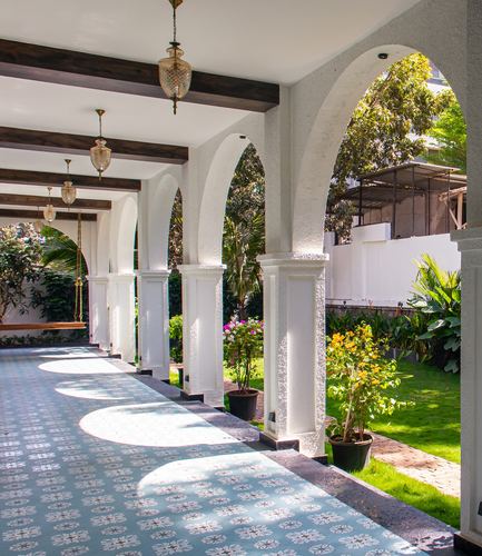 Sunlit arched corridor with patterned tile floor overlooking a garden in a Pune villa
