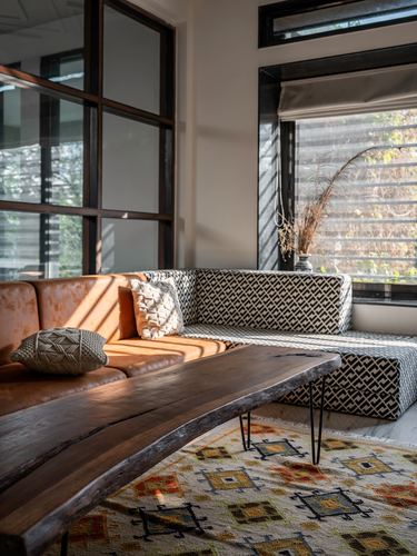 Corner living room with leather and patterned sectional, live-edge wood table, and tall black-framed windows