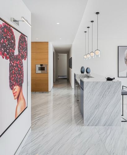 Modern kitchen with marble-look island, staggered pendant lights, and wood-paneled hallway beyond
