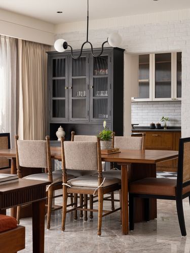 Dining room with wooden table, cane chairs, dark cabinet, and kitchen beyond
