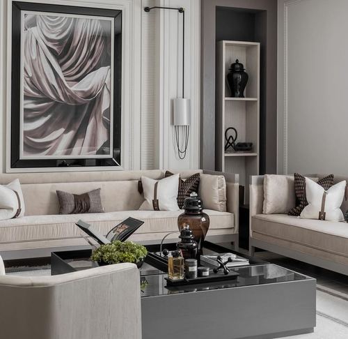 Beige velvet sofas flank a smoked-glass coffee table beneath a large drapery artwork in a neutral living room