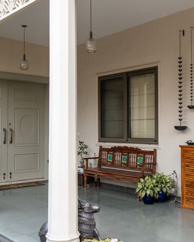 Foyer with stone floor, carved wooden bench, hanging brass diyas, and pillared verandah leading to a grey front door