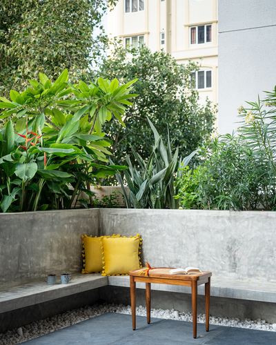 Corner concrete bench with yellow cushions and wooden table on a plant-filled terrace