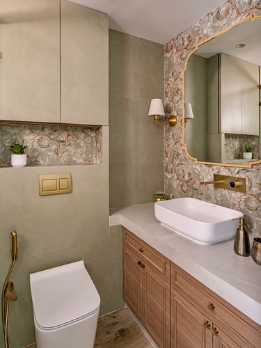 Bathroom with floral wallpaper, arched brass mirror, wood vanity and white vessel sink