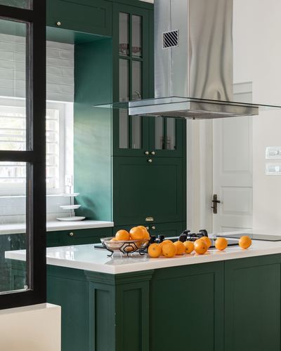 Green shaker kitchen island with white countertop, oranges, and steel chimney hood