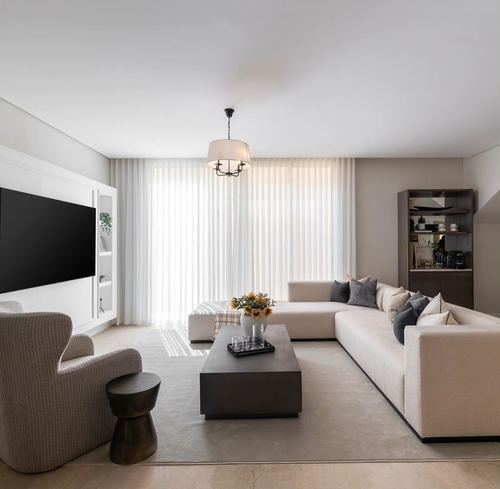 Neutral minimalist living room with sectional sofa, low dark coffee table, and sheer-curtained window
