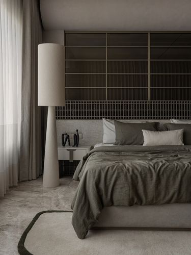 Bedroom with olive linens, cylindrical lamp, and dark paneled wall behind bed