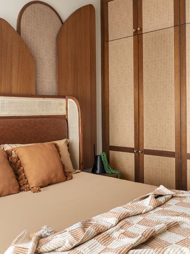 Bed with cane headboard and leather trim beside arched wood-and-cane wall panels and wardrobe