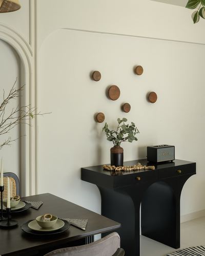 Black console table under wooden wall discs beside dining table with green ceramic plates