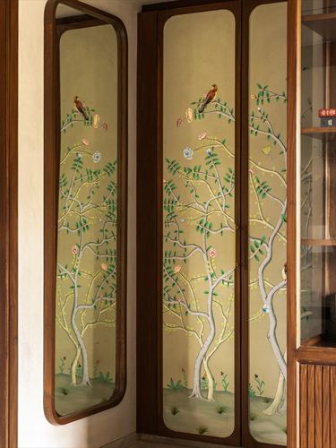 Wooden wardrobe with hand-painted tree and bird mural beside a wood-framed mirror in a foyer.