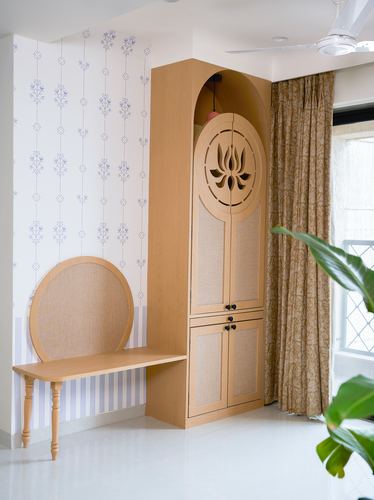Arched wooden wardrobe with carved lotus door beside cane bench and floral wallpaper.