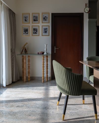 Foyer with turned-leg console, framed photos, wooden door and green velvet chair