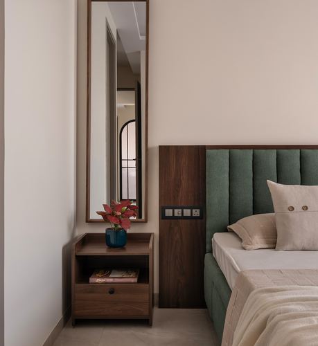 Bedroom corner with green channel-tufted headboard, walnut nightstand, and tall wall mirror