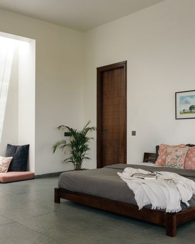 Minimalist bedroom with low wooden bed, panelled wooden door and sunlit reading nook