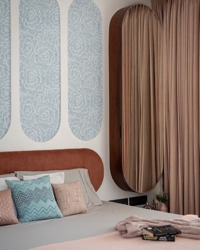 Bedroom corner with terracotta ribbed headboard, blue floral wall panels, and curved wooden wardrobe with oval mirror