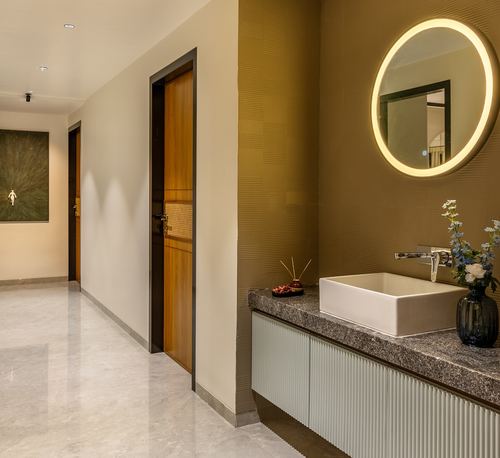 Powder room with round backlit mirror, stone counter, vessel sink, and fluted cabinetry beside a hallway.
