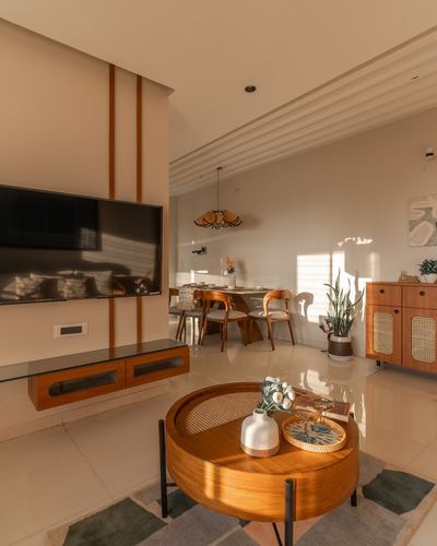 Sunlit living room with wood tv unit, cane sideboard and round wood coffee table opening to dining area