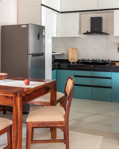 Open kitchen with teal cabinets, black countertop, and wooden dining table with cane chairs