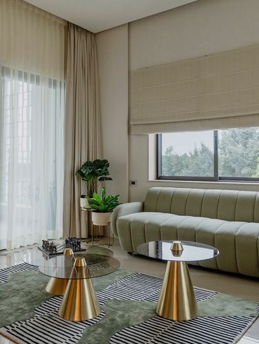 Sage boucle sofa with two brass-based glass coffee tables beside a curtained window