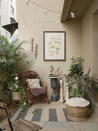 Small terrace corner with rattan chair, botanical print, carved wall masks, plants and woven pouf