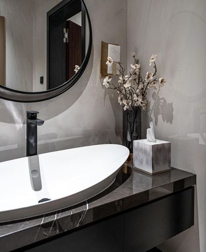 Bathroom vignette with round mirror, black faucet, white vessel sink on dark stone counter
