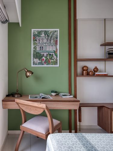 Study nook with green wall, floating teak desk, brass lamp, framed print, and open shelving
