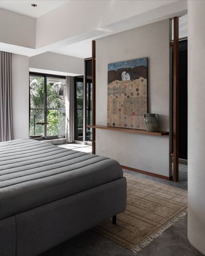 Bedroom with grey channel-tufted bed facing a wood-framed wall art display and window view of greenery