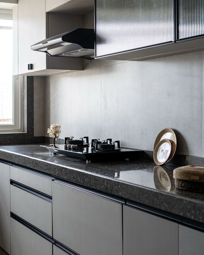 Modern kitchen corner with dark granite counter, black gas hob, chimney hood and fluted glass cabinet.