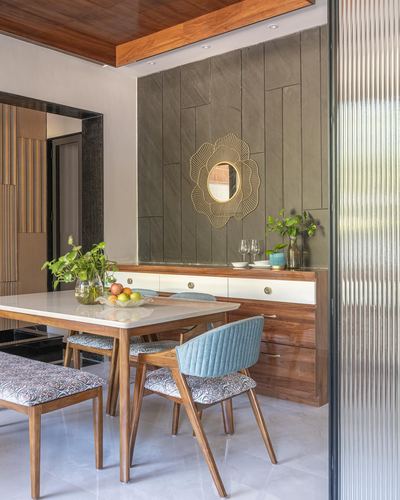 Dining area with wood table, teal chairs, stone accent wall and gold sunburst mirror