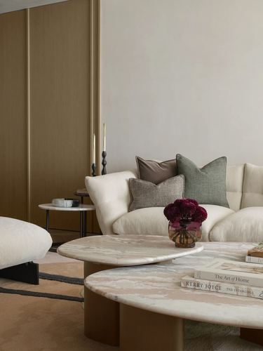 Curved cream sofa with cushions behind layered marble coffee tables and a flower vase