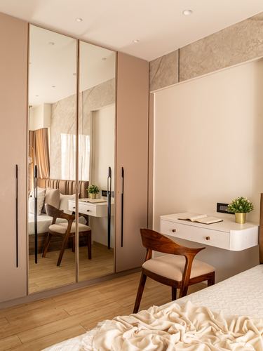 Bedroom with blush pink mirrored wardrobe, floating study desk, and wooden chair on wood flooring