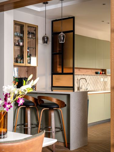Kitchen island with stone waterfall counter, wood bar stools, and glass partition with amber panes.